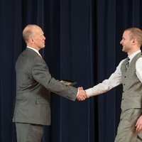 Doctor Potteiger shaking hands with an award recipient in a grey tuxedo vest